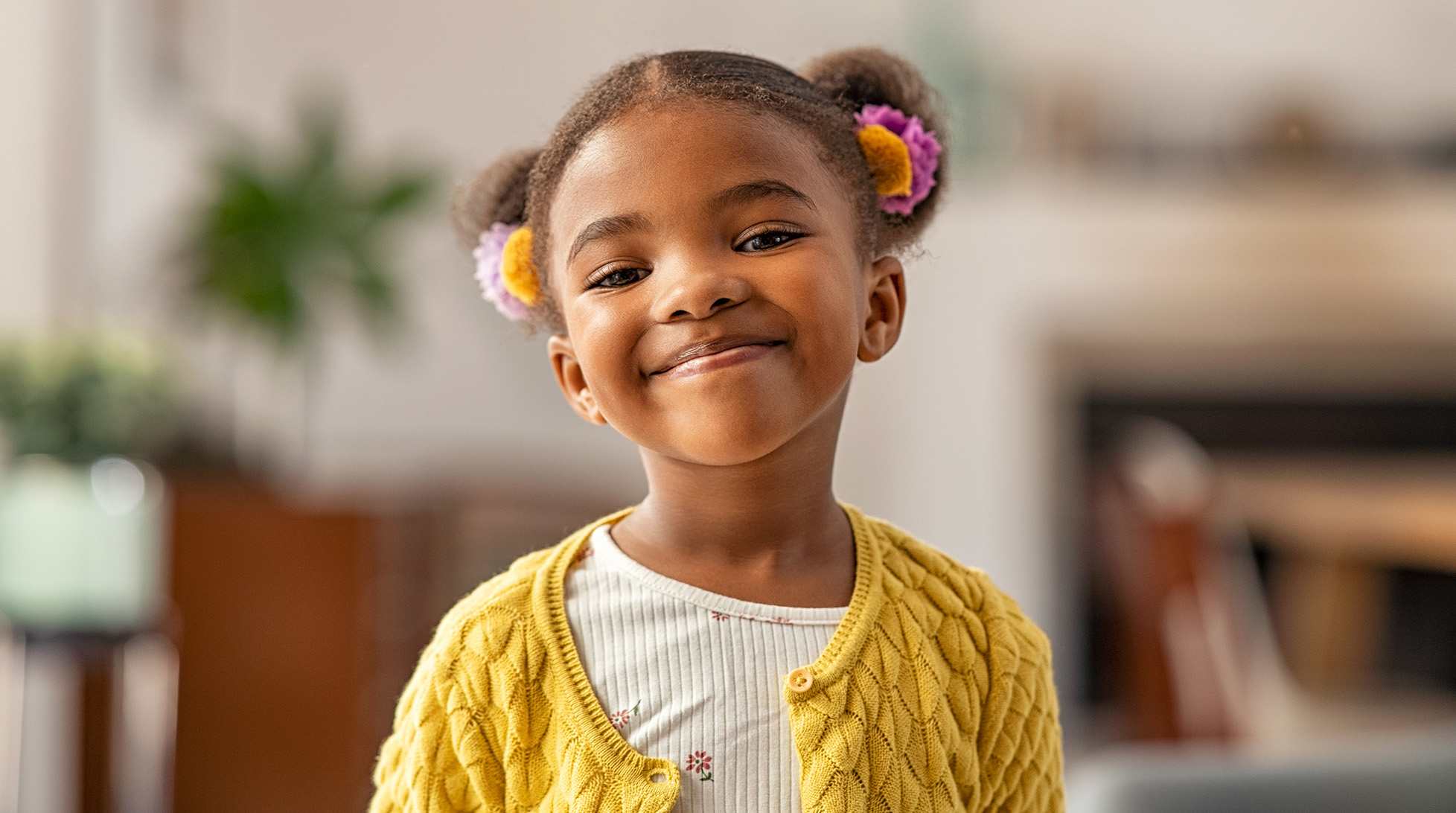 Smiling cute little african american girl with two pony tails looking at camera. Portrait of happy female child at home. Smiling face a of black 4 year old girl looking at camera with afro puff hair.