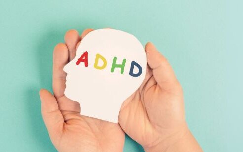hands holding a cut out head with the letters ADHD