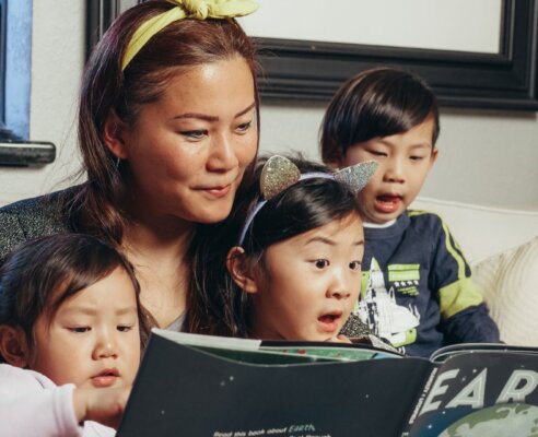 Mom with three kids on lap reading a book