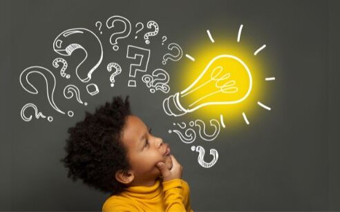 child with doodled questions behind them on a blackboard