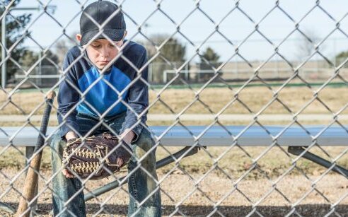 boy with baseball glove sitting behind fence