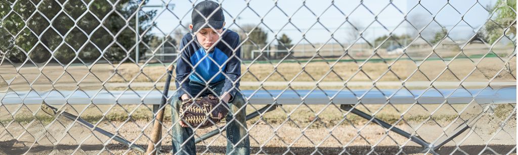 boy with baseball glove sitting behind fence