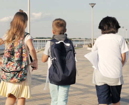 three kids walking by water away from camera