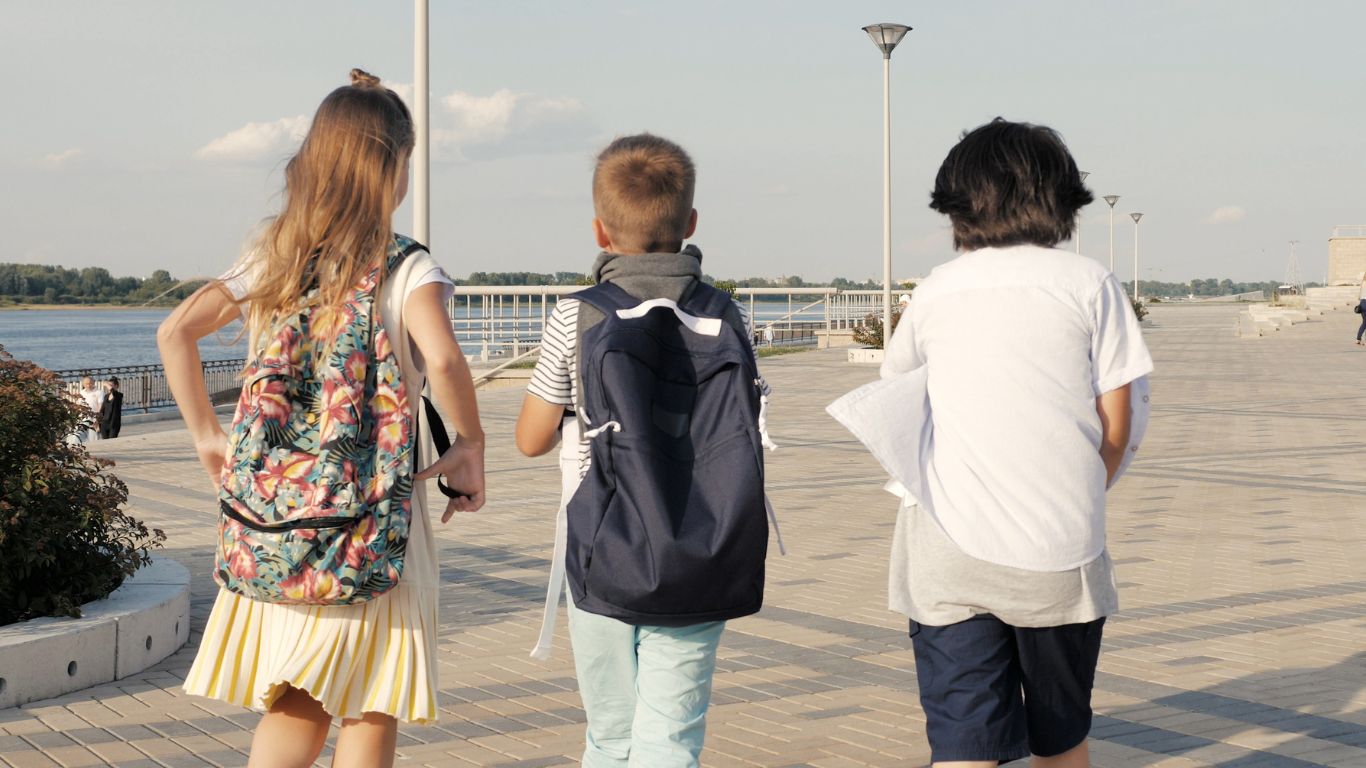 three kids walking by water away from camera
