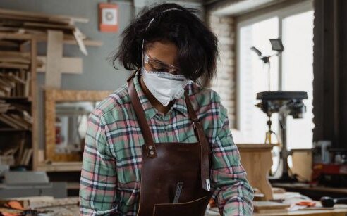 woman in mask at a table cutting wood