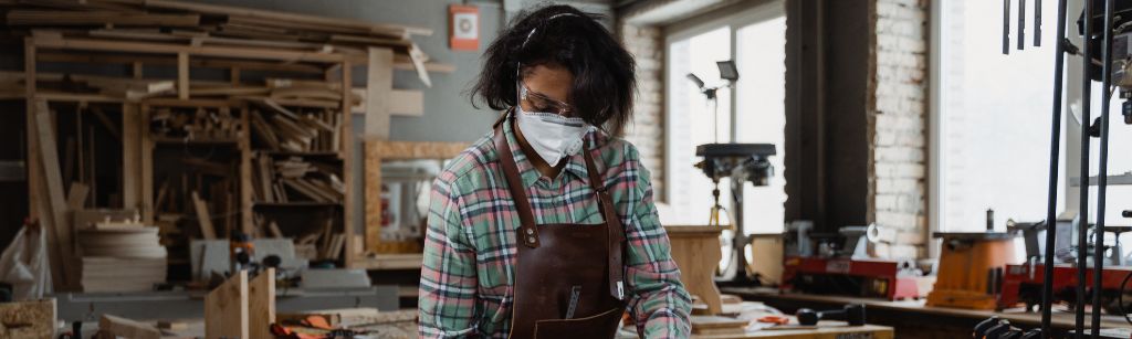 woman in mask at a table cutting wood