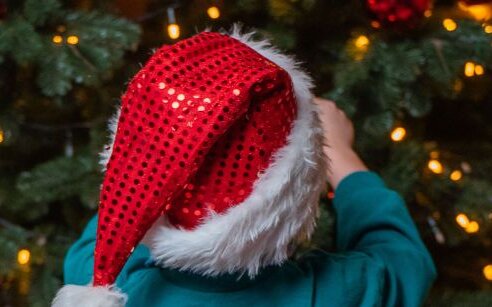 child in red hat decorating a christmas tree